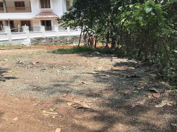 A cleared 21-cent residential land parcel for sale near TK Road, Thiruvalla, featuring level ground and a neighboring modern two-story house.