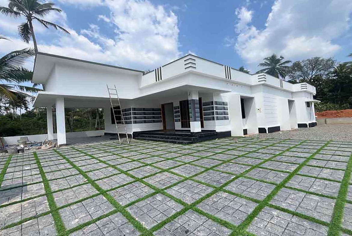 Exterior view of a modern white 3 BHK single-storey gated villa in Thiruvalla with a spacious paved courtyard and contemporary architecture.