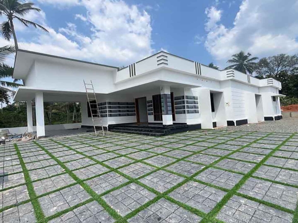 Exterior view of a modern white 3 BHK single-storey gated villa in Thiruvalla with a spacious paved courtyard and contemporary architecture.