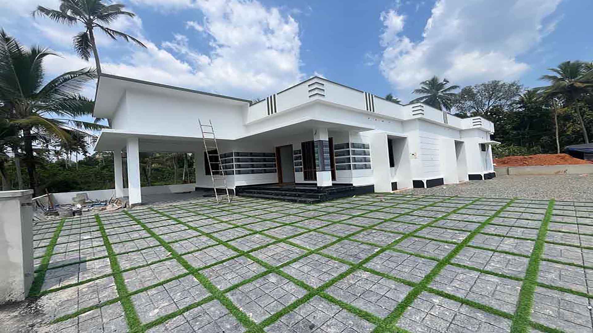 Exterior view of a modern white 3 BHK single-storey gated villa in Thiruvalla with a spacious paved courtyard and contemporary architecture.