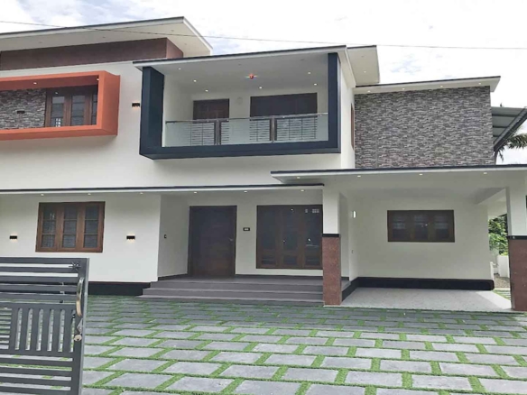 Modern two-storey 4 bedroom house for sale in Thiruvalla Pullad featuring a white exterior, stone cladding, and landscaped front yard with grass pavers.