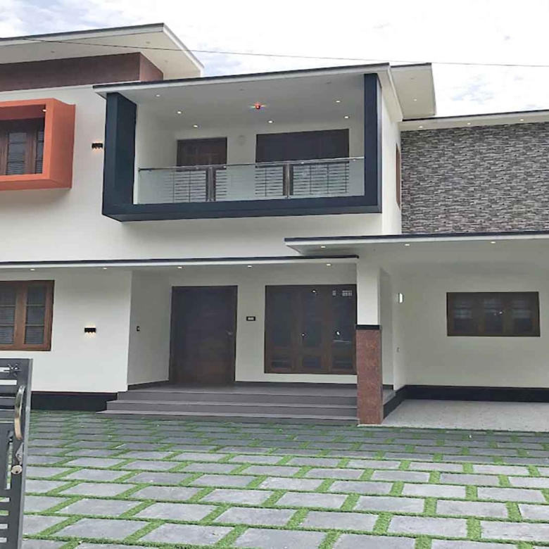 Modern two-storey 4 bedroom house for sale in Thiruvalla Pullad featuring a white exterior, stone cladding, and landscaped front yard with grass pavers.