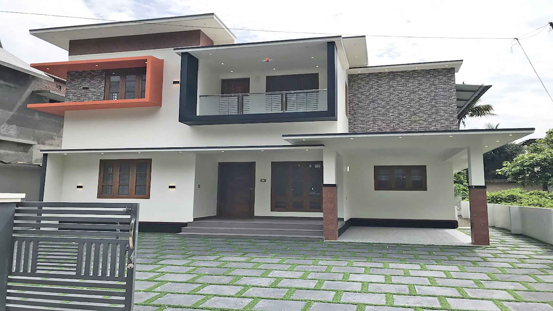 Modern two-storey 4 bedroom house for sale in Thiruvalla Pullad featuring a white exterior, stone cladding, and landscaped front yard with grass pavers.