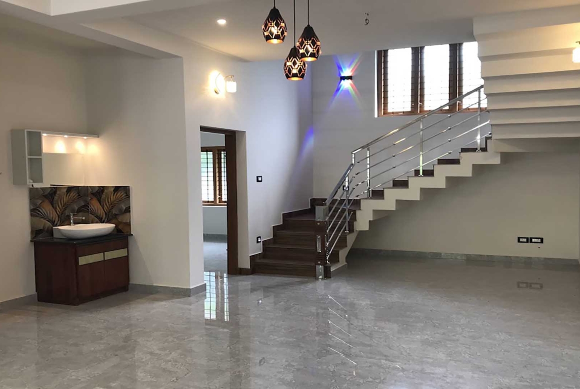 Interior of a 4 bedroom house for sale in Thiruvalla featuring a modern open-plan dining area, stylish wash basin with vanity, and a contemporary staircase with stainless steel railings.