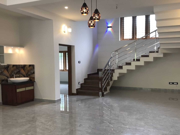 Interior of a 4 bedroom house for sale in Thiruvalla featuring a modern open-plan dining area, stylish wash basin with vanity, and a contemporary staircase with stainless steel railings.