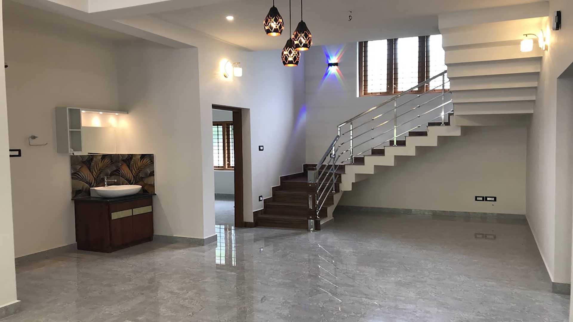 Interior of a 4 bedroom house for sale in Thiruvalla featuring a modern open-plan dining area, stylish wash basin with vanity, and a contemporary staircase with stainless steel railings.