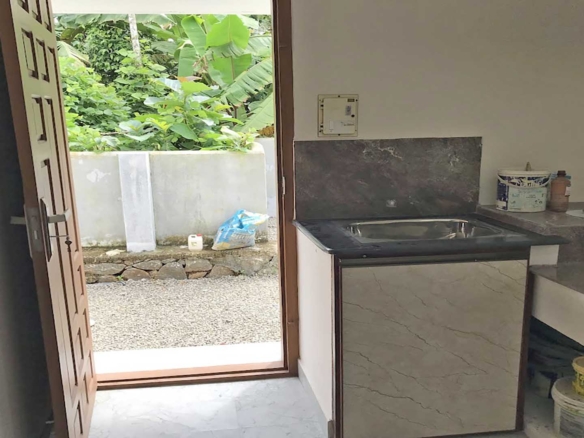 Spacious kitchen work area and utility space with a stainless steel sink, granite countertop, and backyard access in a 4-bedroom house for sale in Thiruvalla.