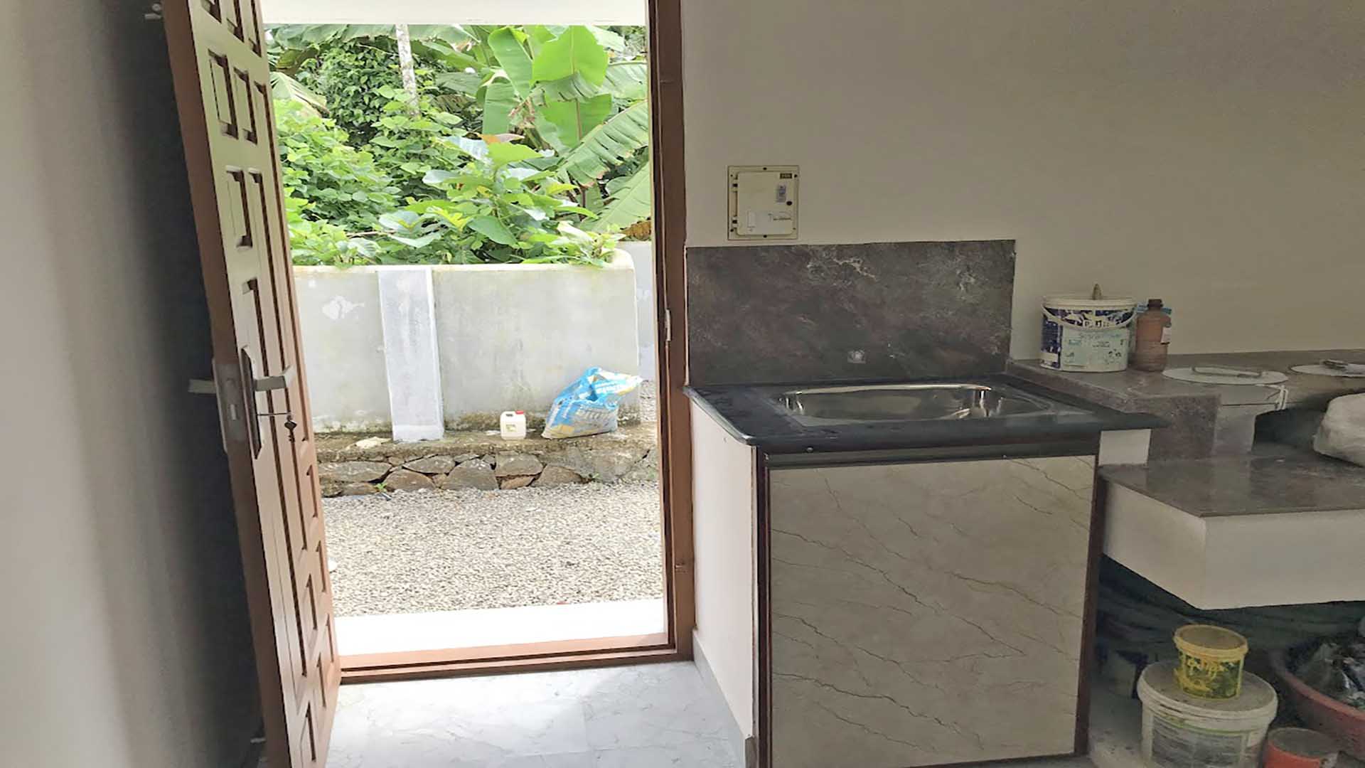 Spacious kitchen work area and utility space with a stainless steel sink, granite countertop, and backyard access in a 4-bedroom house for sale in Thiruvalla.