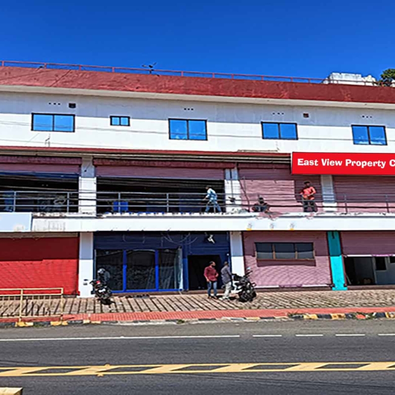 Wide-angle shot of a three-story commercial building for sale on MC Road, Chengannur, featuring multiple retail storefronts and upper-floor office spaces.