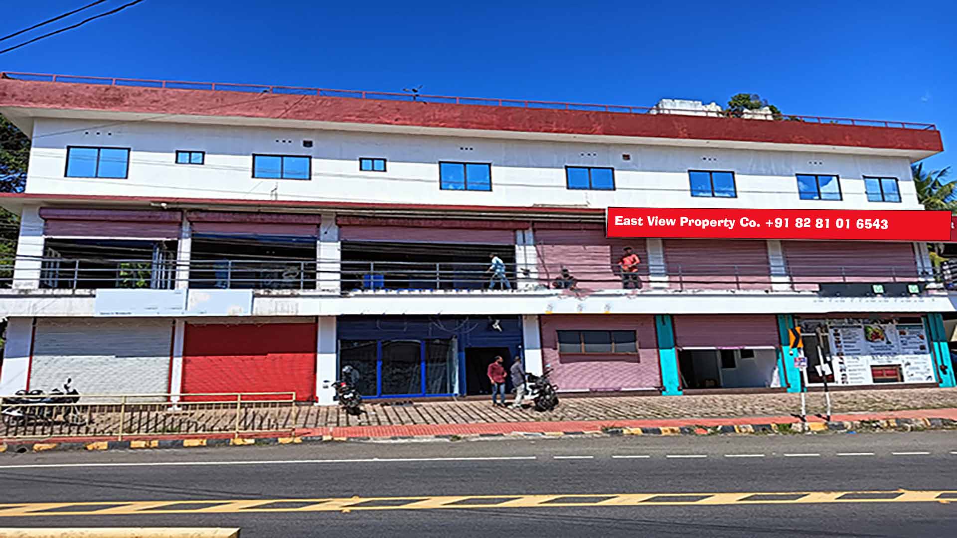 Wide-angle shot of a three-story commercial building for sale on MC Road, Chengannur, featuring multiple retail storefronts and upper-floor office spaces.