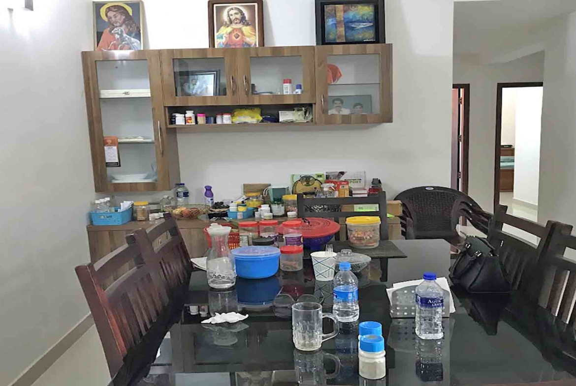 A modern dining room featuring a dark wood dining table with a glass top, matching wooden chairs, and a wall-mounted wooden crockery cabinet with glass doors.
