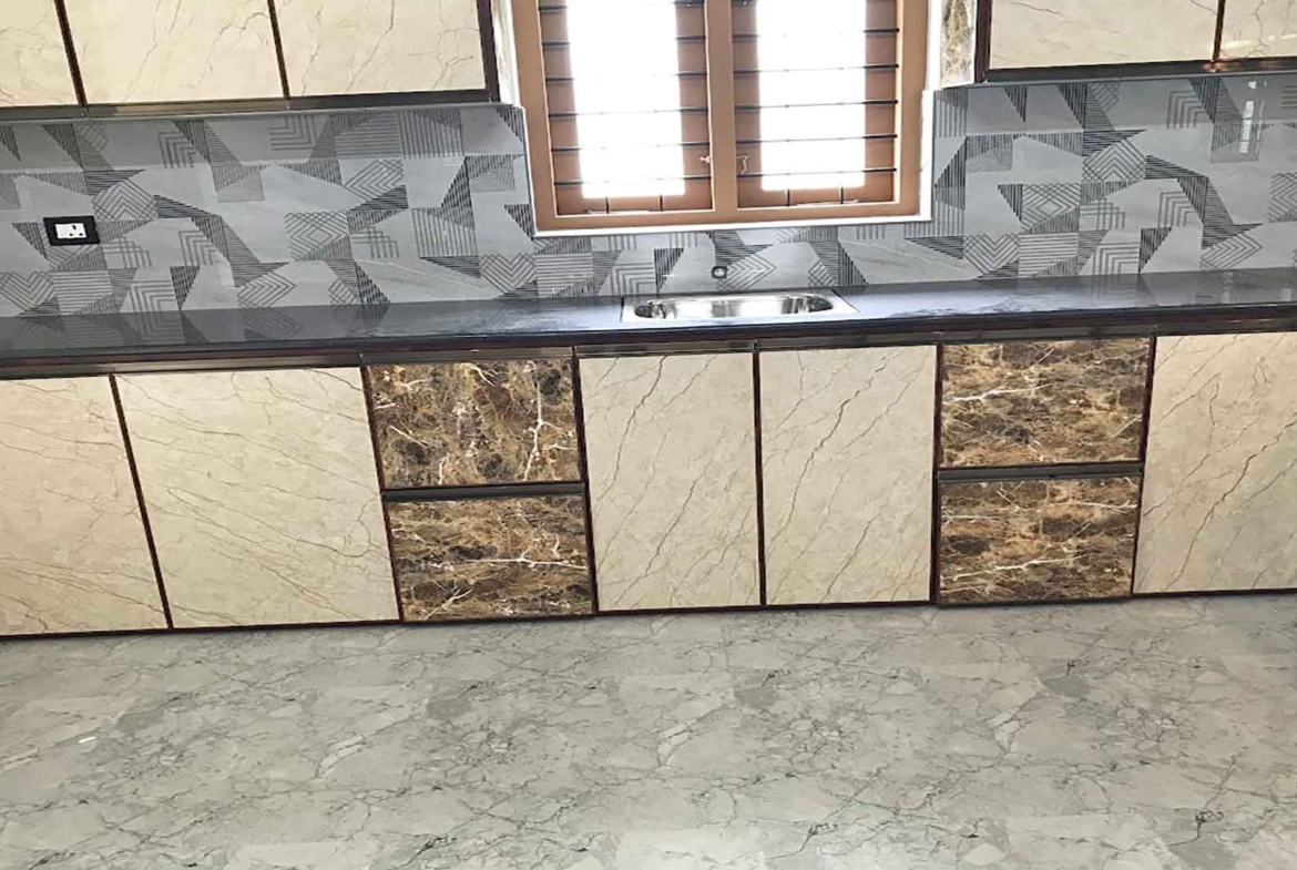 Modern modular kitchen in a 4 bedroom house for sale in Pullad, Thiruvalla, featuring marble-finish cabinets, a black granite countertop, and geometric backsplash tiles.