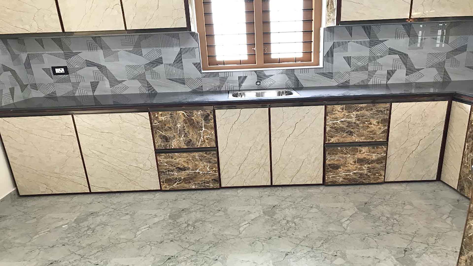 Modern modular kitchen in a 4 bedroom house for sale in Pullad, Thiruvalla, featuring marble-finish cabinets, a black granite countertop, and geometric backsplash tiles.