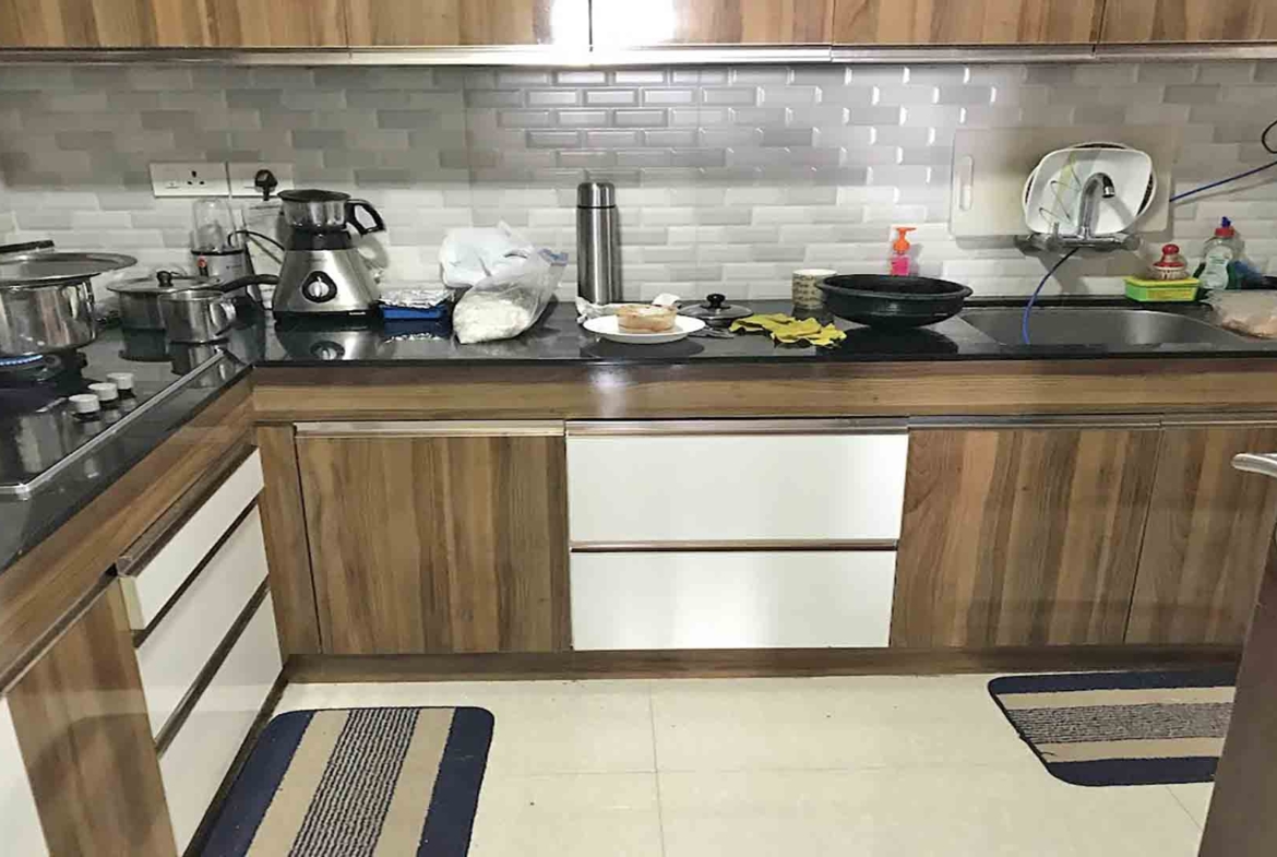 A modern L-shaped modular kitchen featuring wood-grain and white cabinetry, a black granite countertop, and a light gray subway tile backsplash.