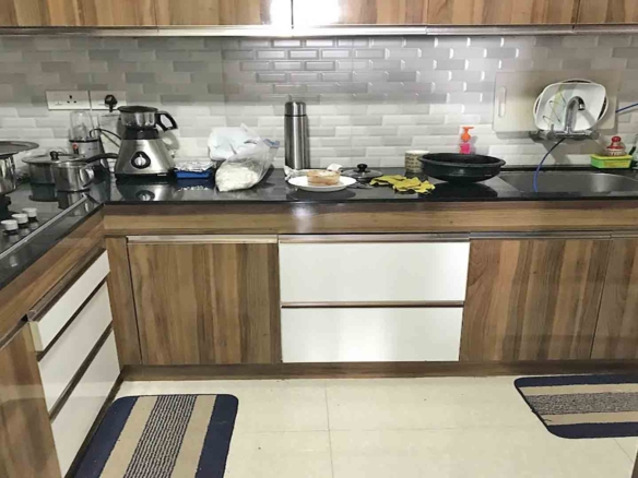 A modern L-shaped modular kitchen featuring wood-grain and white cabinetry, a black granite countertop, and a light gray subway tile backsplash.