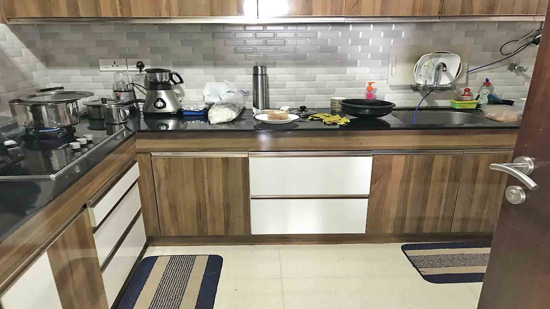A modern L-shaped modular kitchen featuring wood-grain and white cabinetry, a black granite countertop, and a light gray subway tile backsplash.