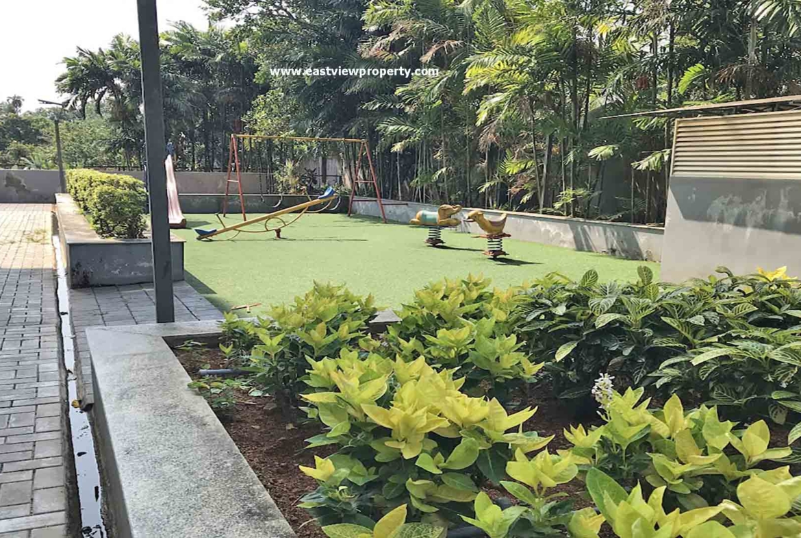 Outside view of the amenities at The Edge by Skyline, Tiruvalla, showing a children's play area with swings and a seesaw on green turf.