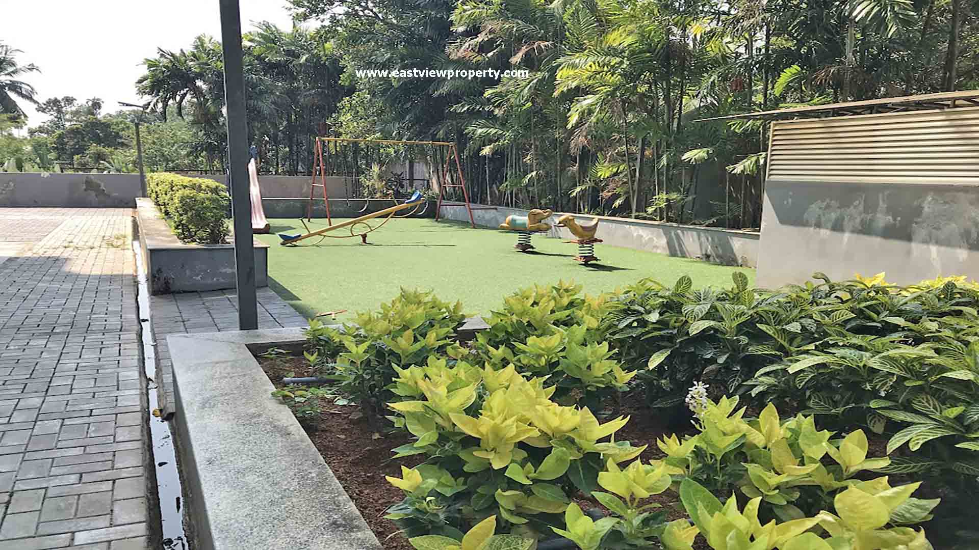 Outside view of the amenities at The Edge by Skyline, Tiruvalla, showing a children's play area with swings and a seesaw on green turf.