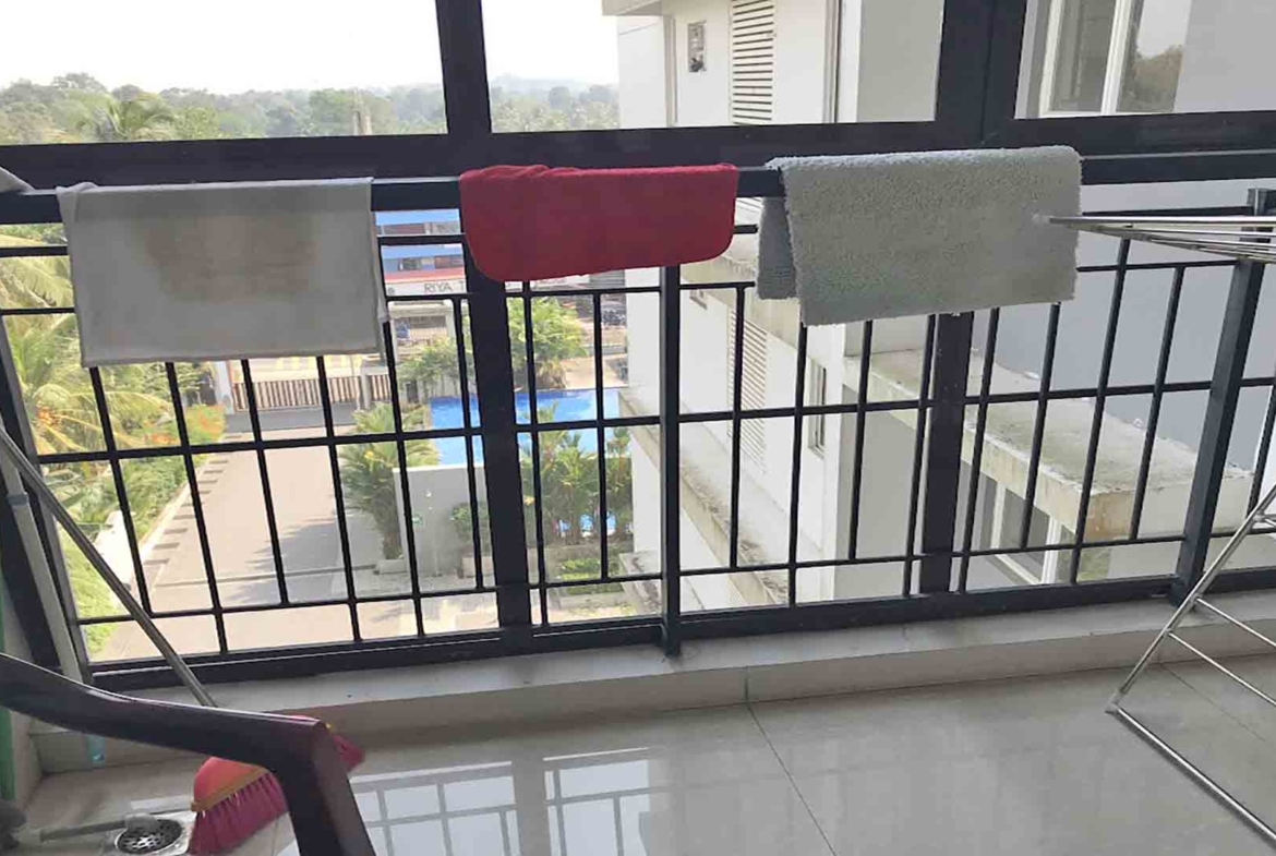 Balcony of a furnished 3 BHK flat at The Edge by Skyline in Tiruvalla, featuring a metal railing, drying rack, and a view of the building complex and pool.