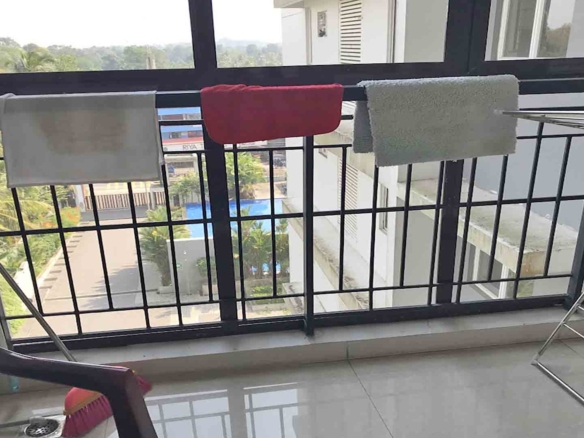 Balcony of a furnished 3 BHK flat at The Edge by Skyline in Tiruvalla, featuring a metal railing, drying rack, and a view of the building complex and pool.