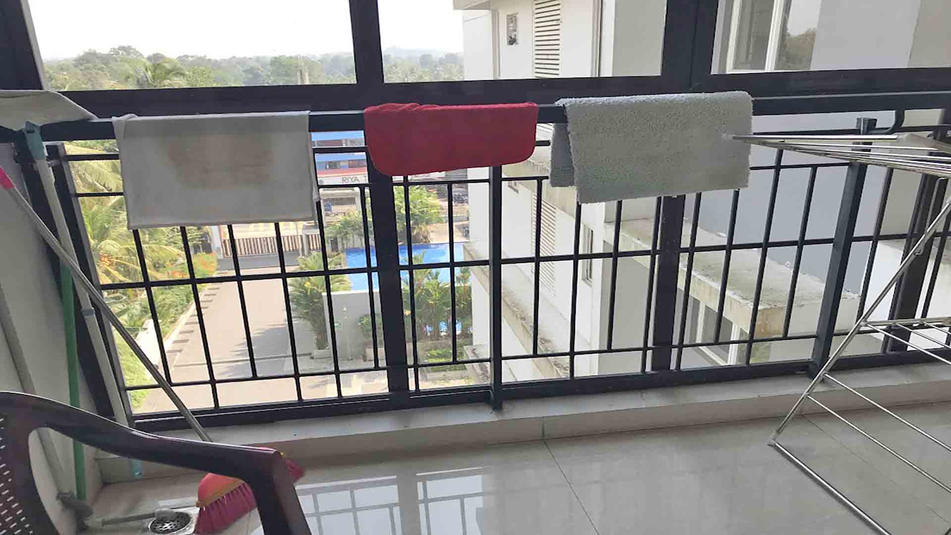 Balcony of a furnished 3 BHK flat at The Edge by Skyline in Tiruvalla, featuring a metal railing, drying rack, and a view of the building complex and pool.