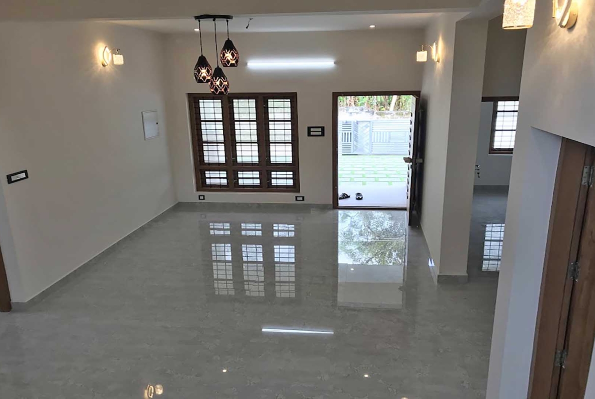 Spacious living room interior of a 2-storey house for sale in Thiruvalla, featuring high-gloss flooring, modern pendant lighting, and an open-plan layout.