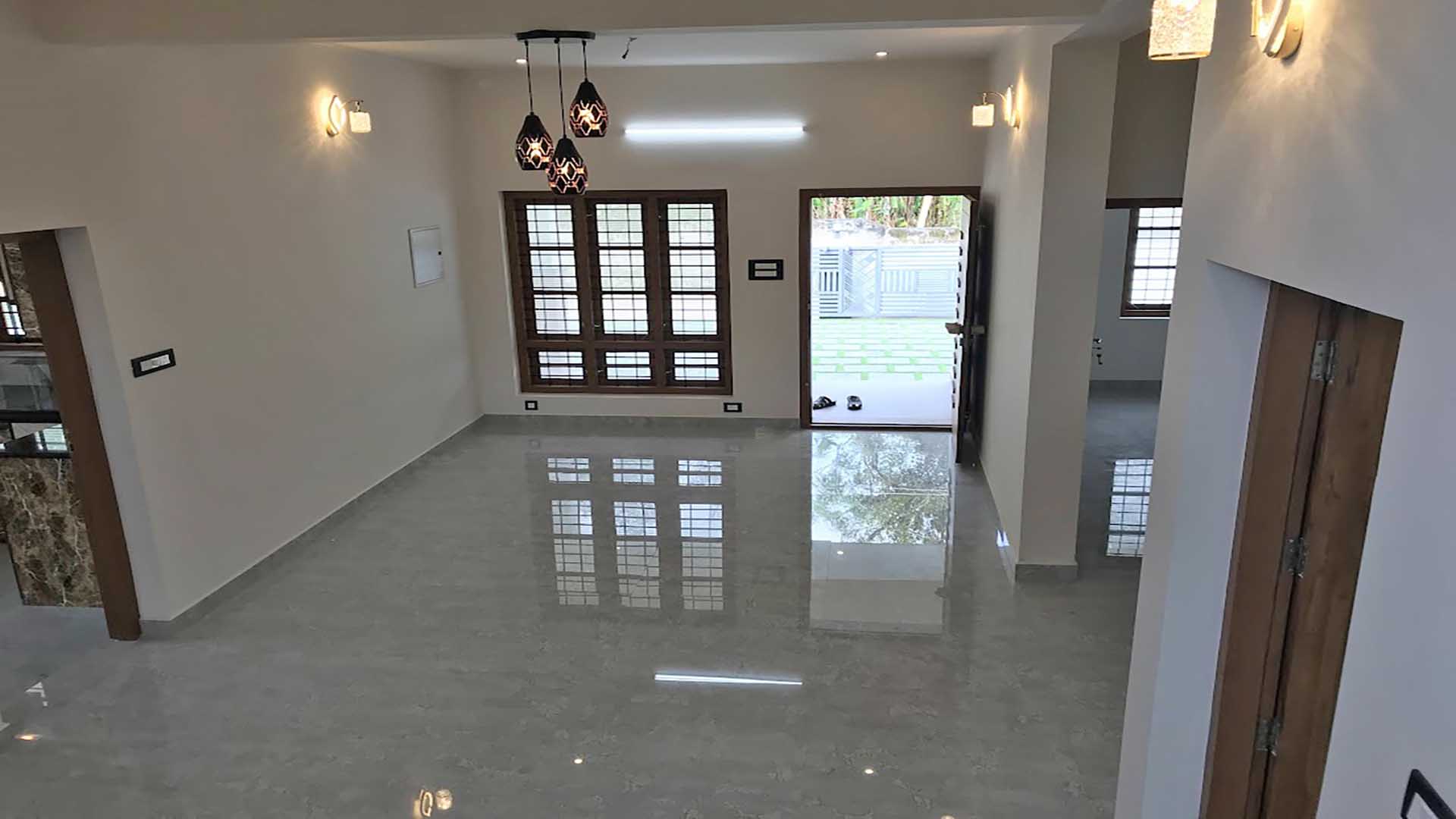 Spacious living room interior of a 2-storey house for sale in Thiruvalla, featuring high-gloss flooring, modern pendant lighting, and an open-plan layout.