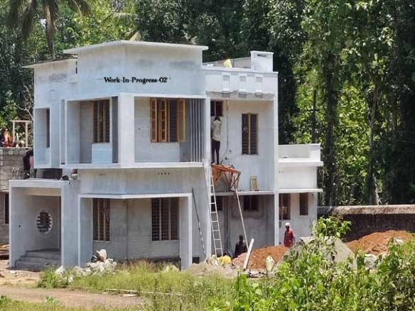 Side-front view of a 4 BHK two-storey house under construction on 8 cents of land in Kumbanad, Thiruvalla. The background includes coconut and other trees.