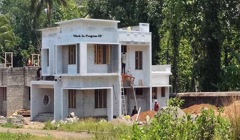 Side-front view of a 4 BHK two-storey house under construction on 8 cents of land in Kumbanad, Thiruvalla. The background includes coconut and other trees.