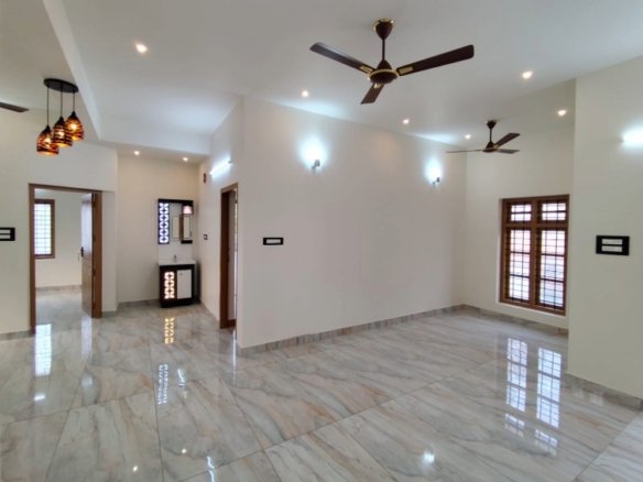 Large front living hall in a 3 BHK villa in Thiruvalla, featuring premium glazed vitrified flooring, false ceiling spot lighting, and dual ceiling fans.
