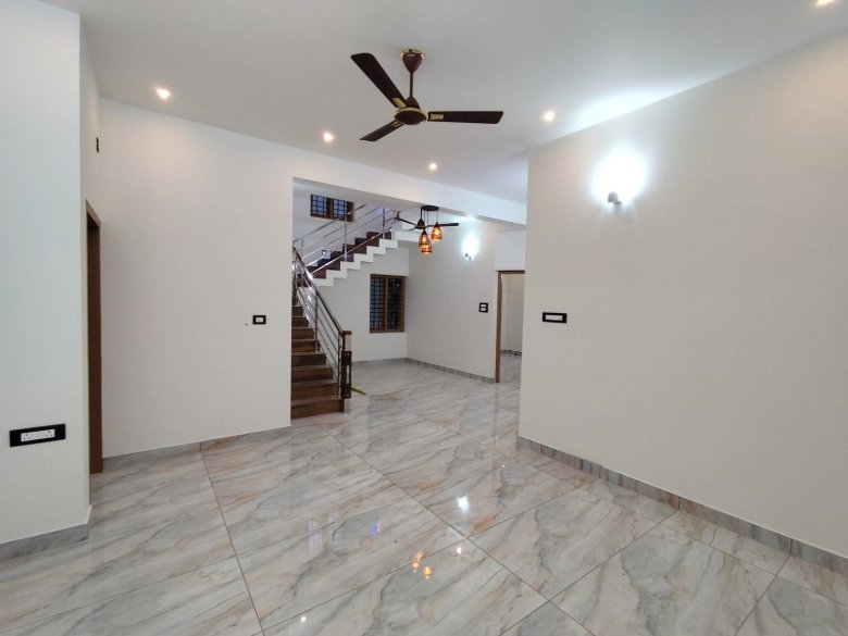 Modern living area with an internal staircase in a 1850 sq ft 3 BHK villa near Eraviperoor Junction, Thiruvalla, featuring premium tiled flooring and open-concept design.