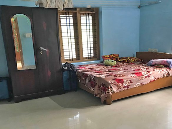 Well-lit bedroom interior with blue-coloured wall, wooden-framed windows and mirror-fitted cupboard, in a single-storey 2 BHK house in Kareelamukk, Thiruvalla