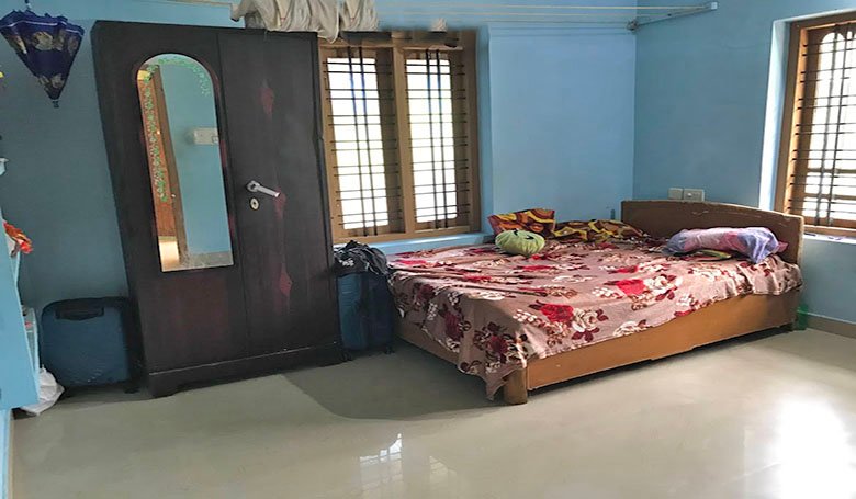 Well-lit bedroom interior with blue-coloured wall, wooden-framed windows and mirror-fitted cupboard, in a single-storey 2 BHK house in Kareelamukk, Thiruvalla