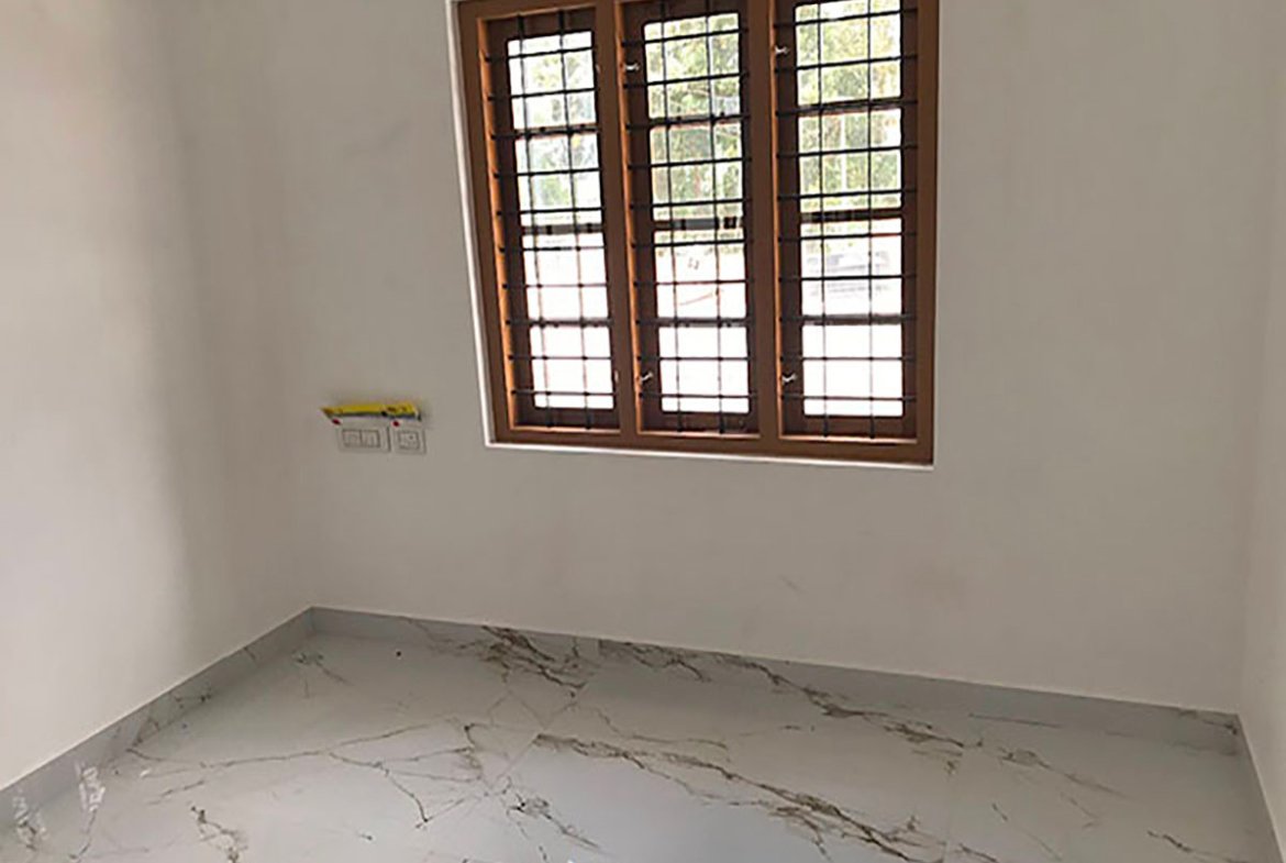 Airy bedroom with a three-pane wooden window, iron safety grills, electrical points, and glossy marbled floor.