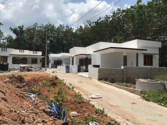 Three contemporary white villas lined up along a common paved access road surrounded by green trees.