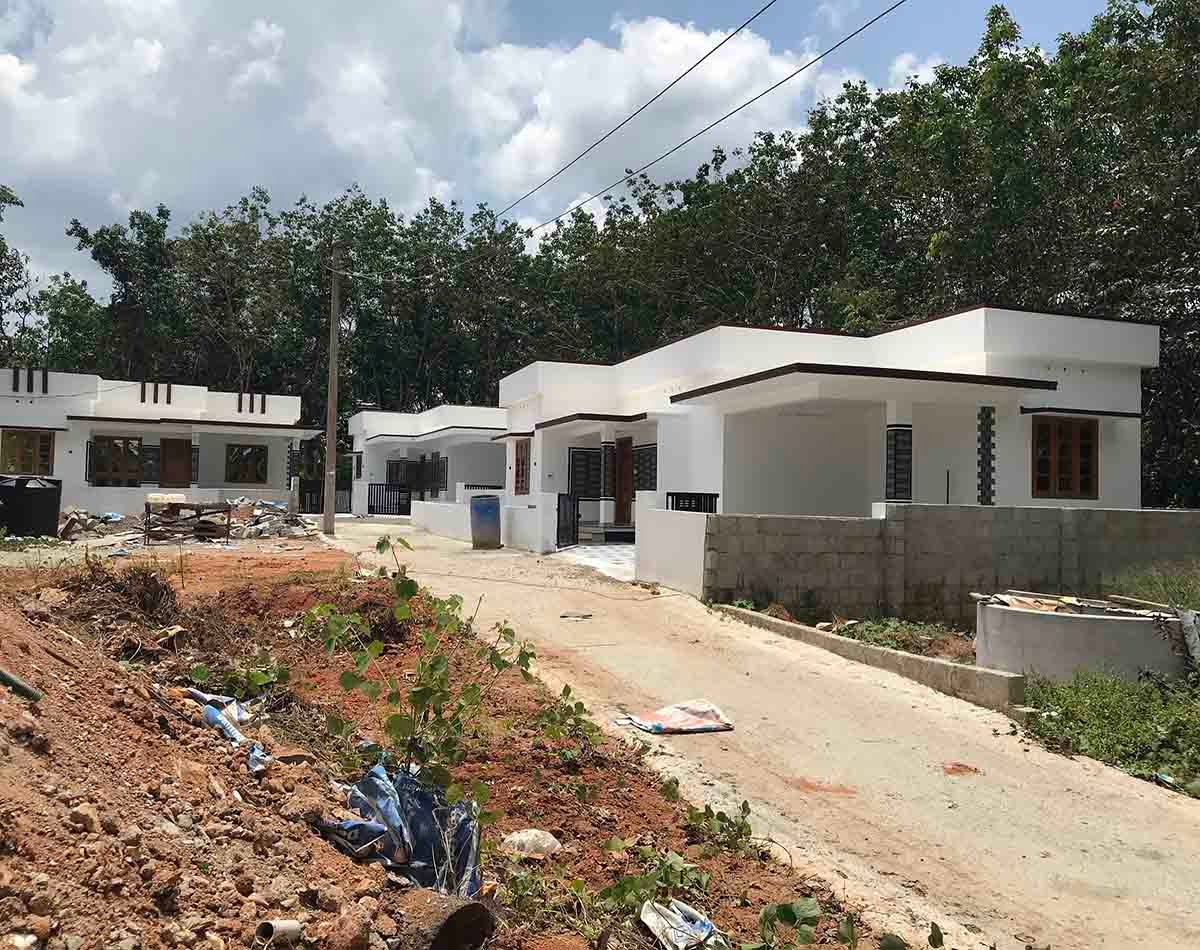 gated-villa-project-3-houses-thiruvalla-kumbanad Three contemporary white villas lined up along a common paved access road surrounded by green trees.