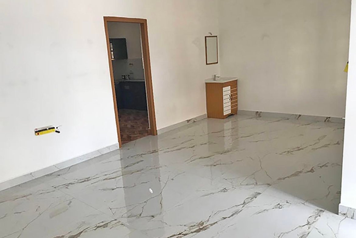 Spacious villa living room with glossy marble-look floor tiles, kitchen doorway, and washbasin vanity.