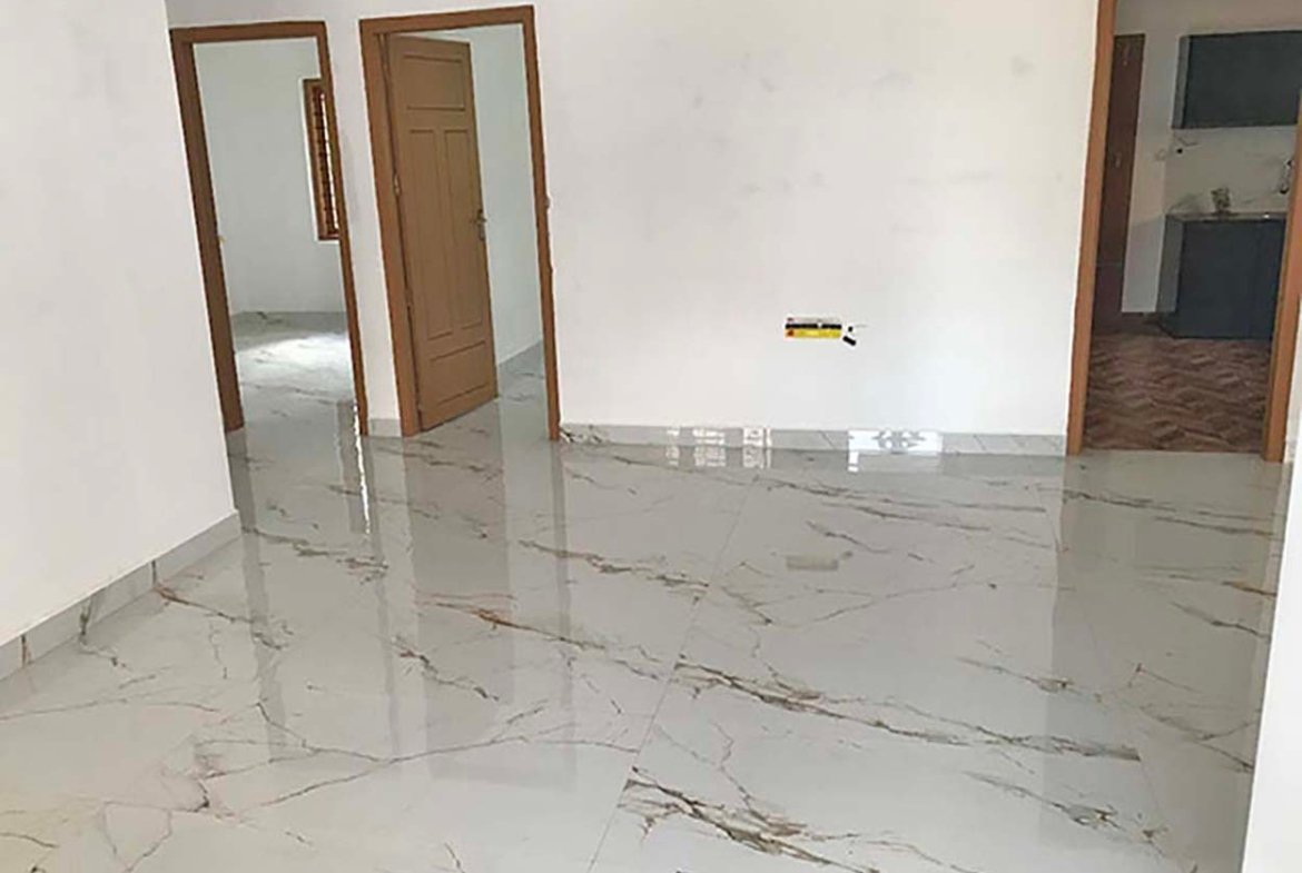 Wide living hall with polished marble-look flooring and wooden doors leading to bedrooms and kitchen.