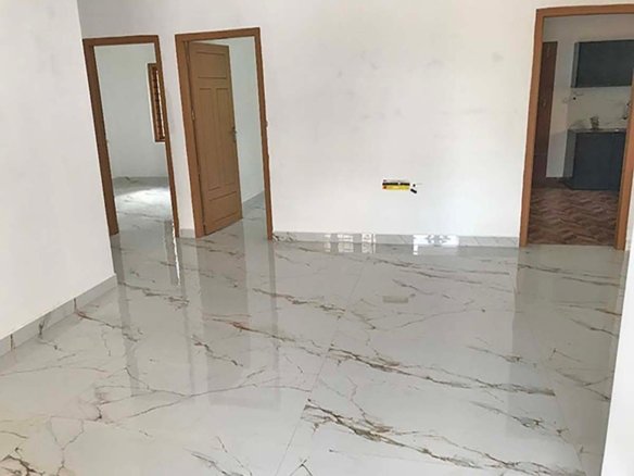 Wide living hall with polished marble-look flooring and wooden doors leading to bedrooms and kitchen.