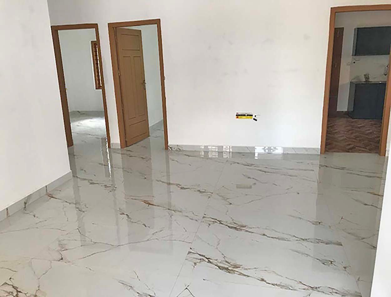 living-area-02 Wide living hall with polished marble-look flooring and wooden doors leading to bedrooms and kitchen.