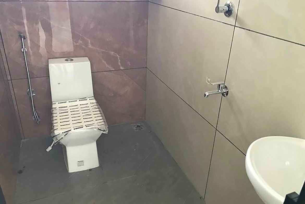 Modern bathroom with floor-mounted water closet, health faucet, chrome fixtures, ceramic washbasin, and tiled walls.